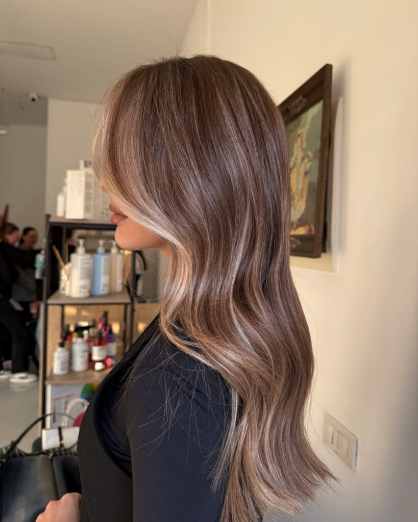 A woman in profile shows off long wavy ash brown hair featuring a bright platinum face-framing highlight.