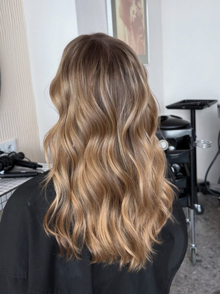 A back view of long wavy sandy blonde hair with rich honey and golden highlights throughout.