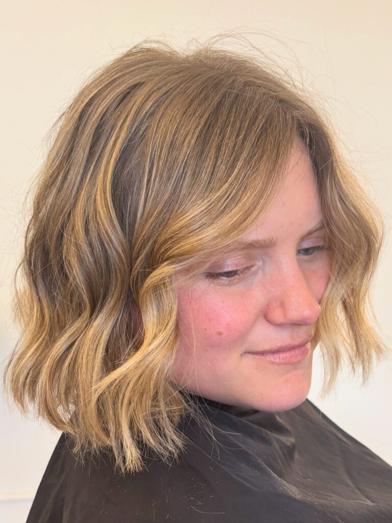 A woman from a slight side angle showing a chin length golden blonde textured bob haircut styled in beachy waves.