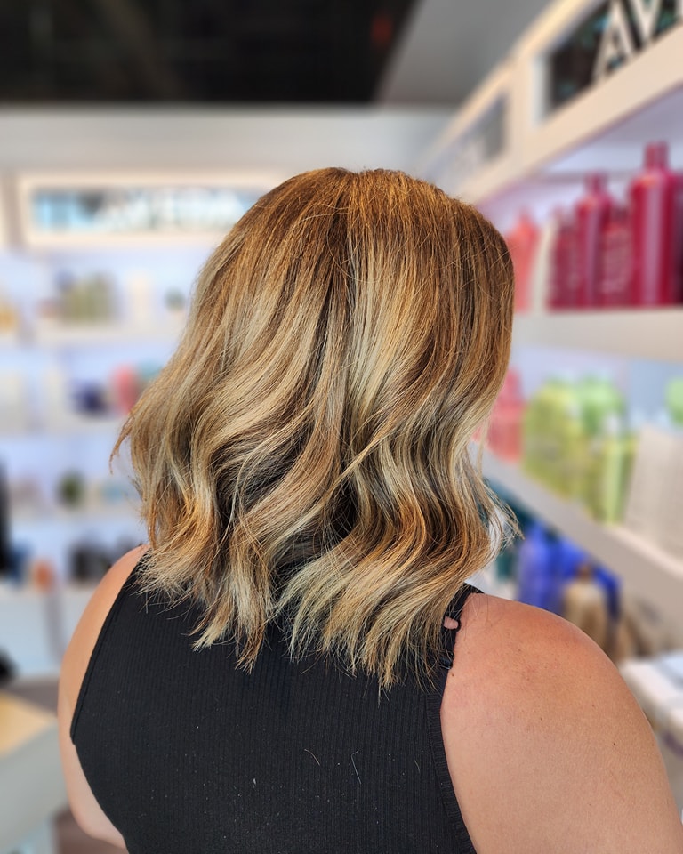 A woman from the back showing a shoulder length caramel blonde layered haircut with soft waves.