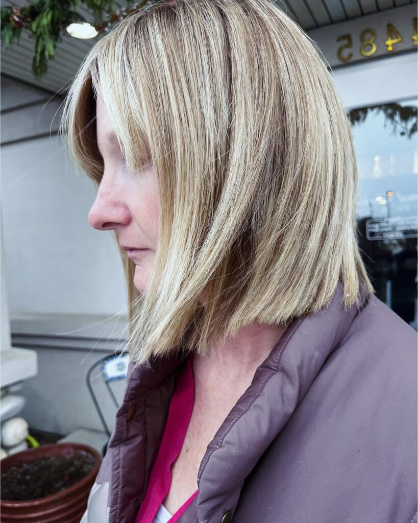 A woman with straight shoulder length hair featuring a dimensional champagne blonde color and soft layers.
