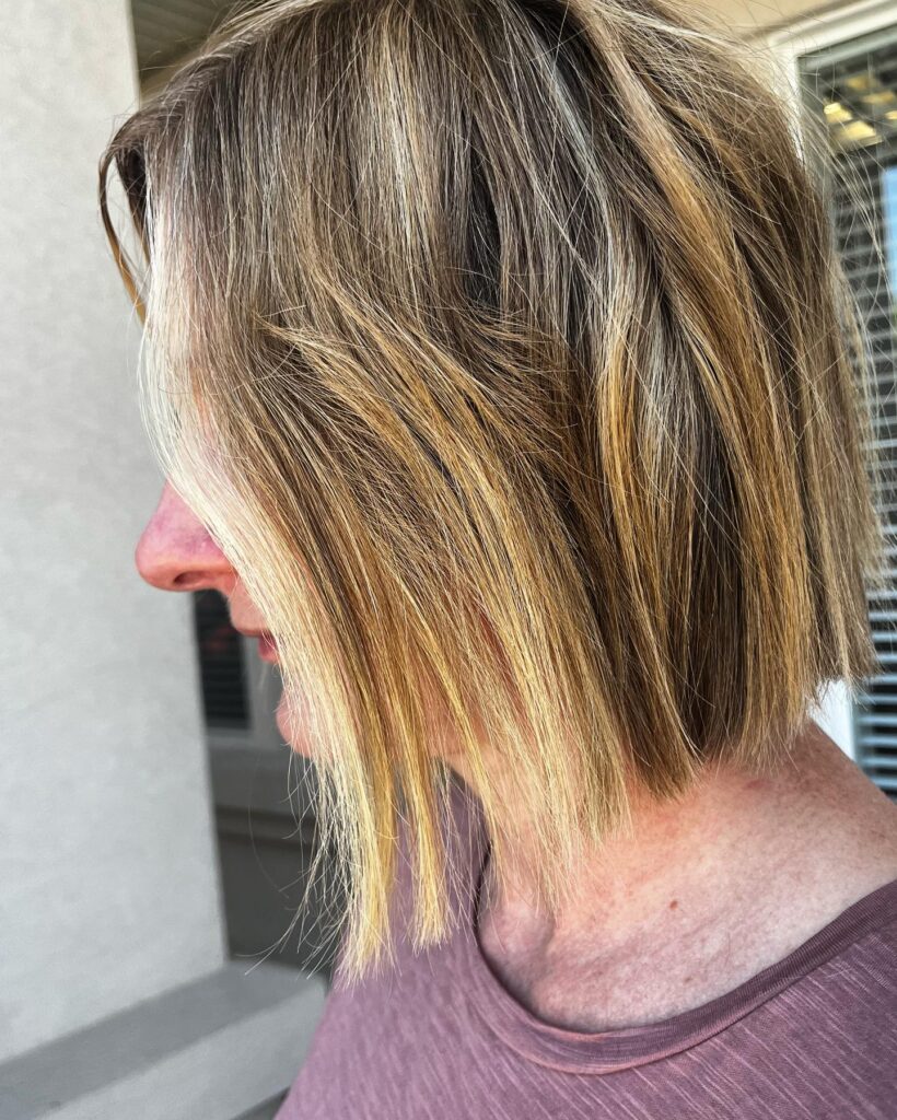 A woman with a straight chin length bob featuring dimensional golden blonde balayage and soft face framing layers.
