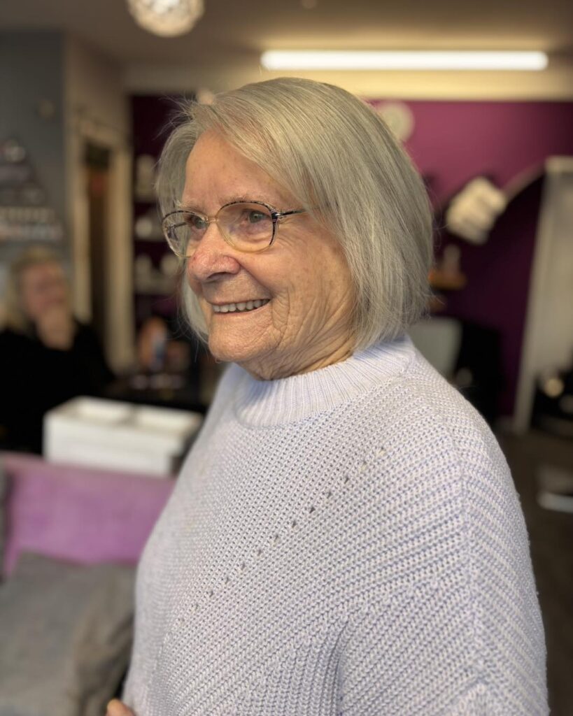 An older woman smiling and wearing a soft chin length silver bob with a side part and rounded ends.