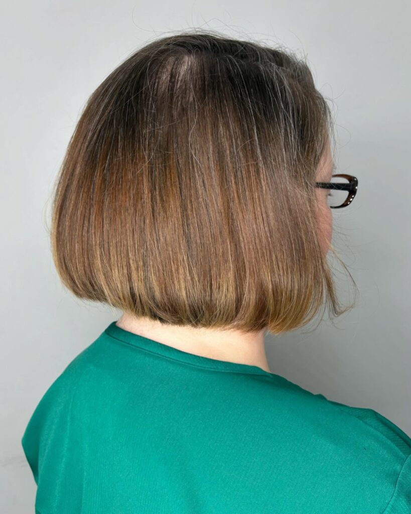A back view of a woman with a straight chin length inverted bob in a warm brown color with golden highlights at the ends.