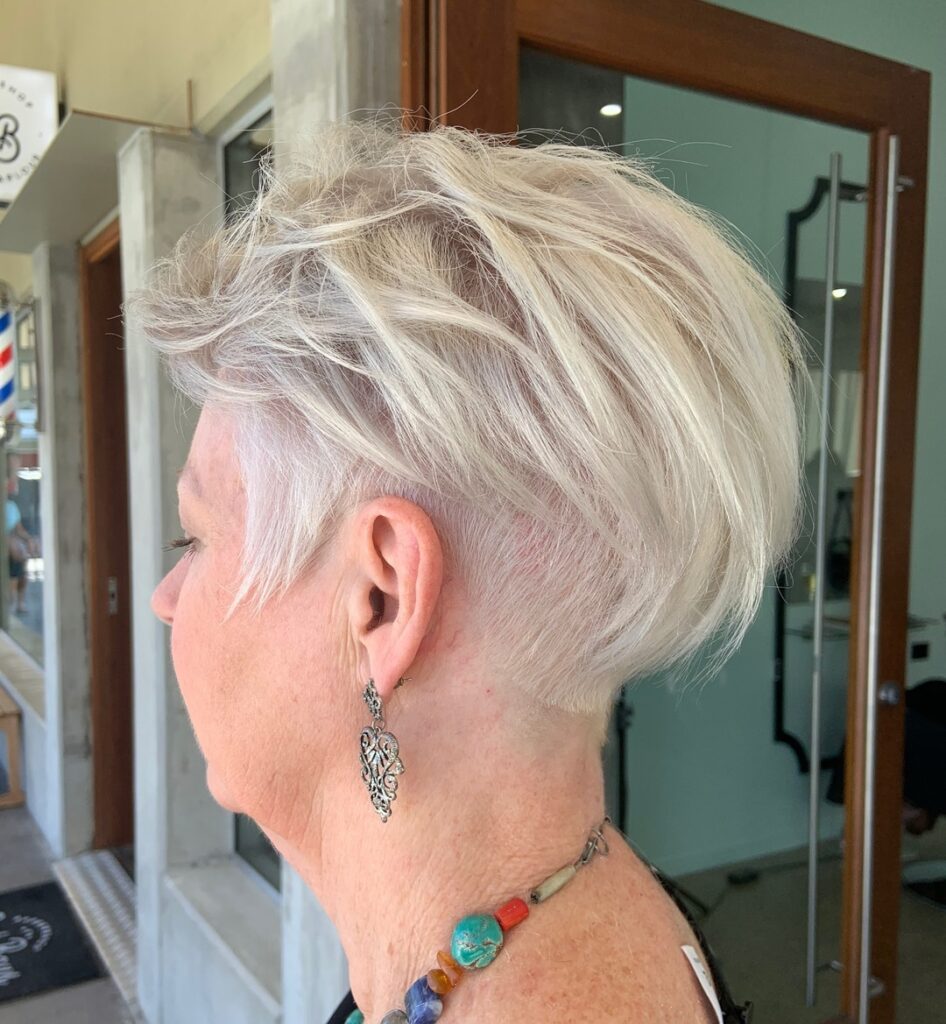 A woman with a round face features a spiky platinum pixie cut with short tapered sides and voluminous textured layers on top.