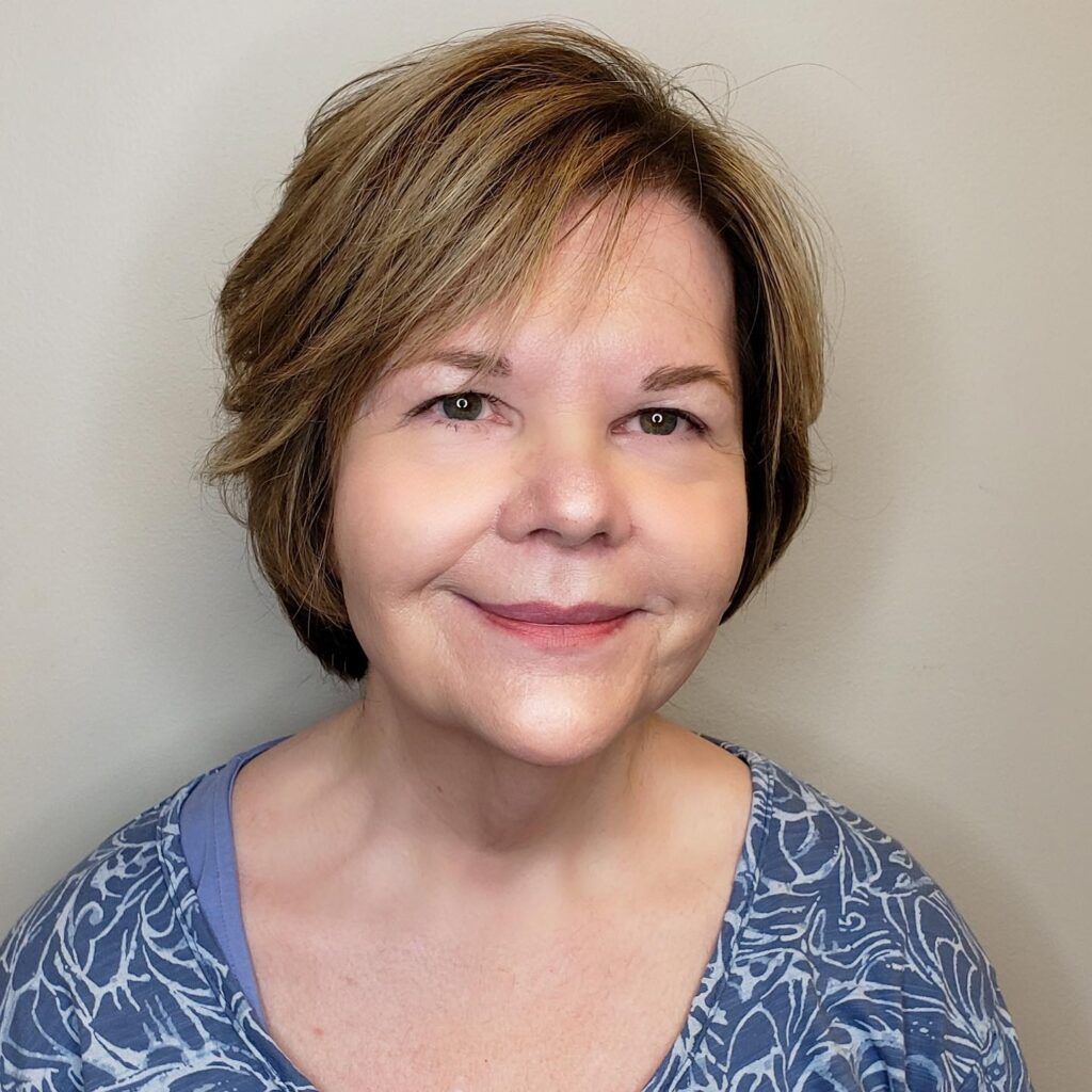 A woman with a round face shape wearing a textured silver pixie cut with voluminous feathery layers on top.