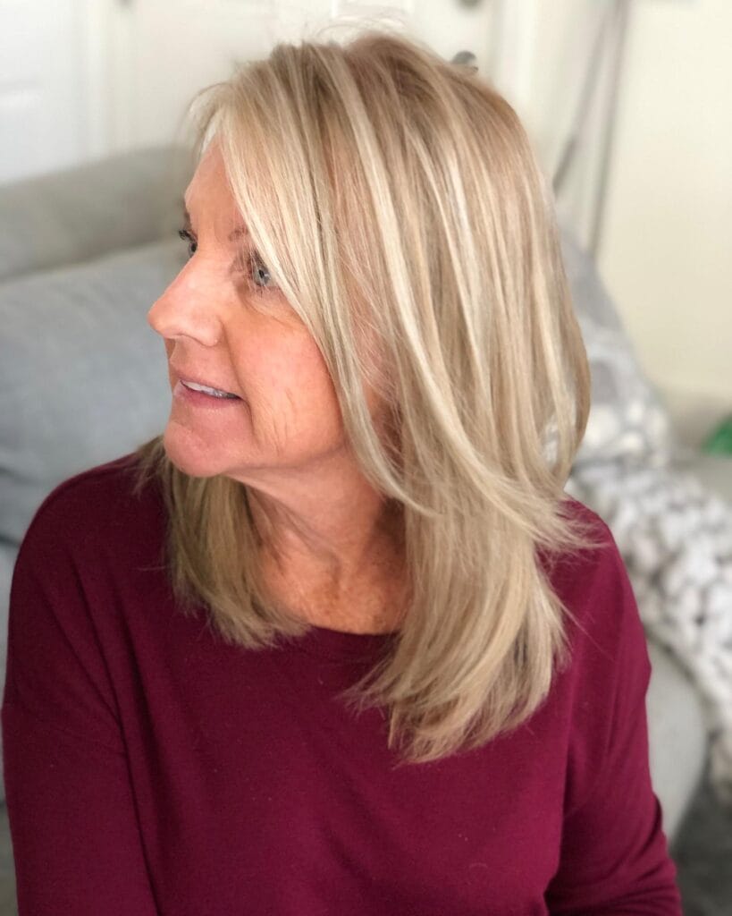 A woman with a shoulder length champagne blonde hairstyle featuring sleek layers and a side part.