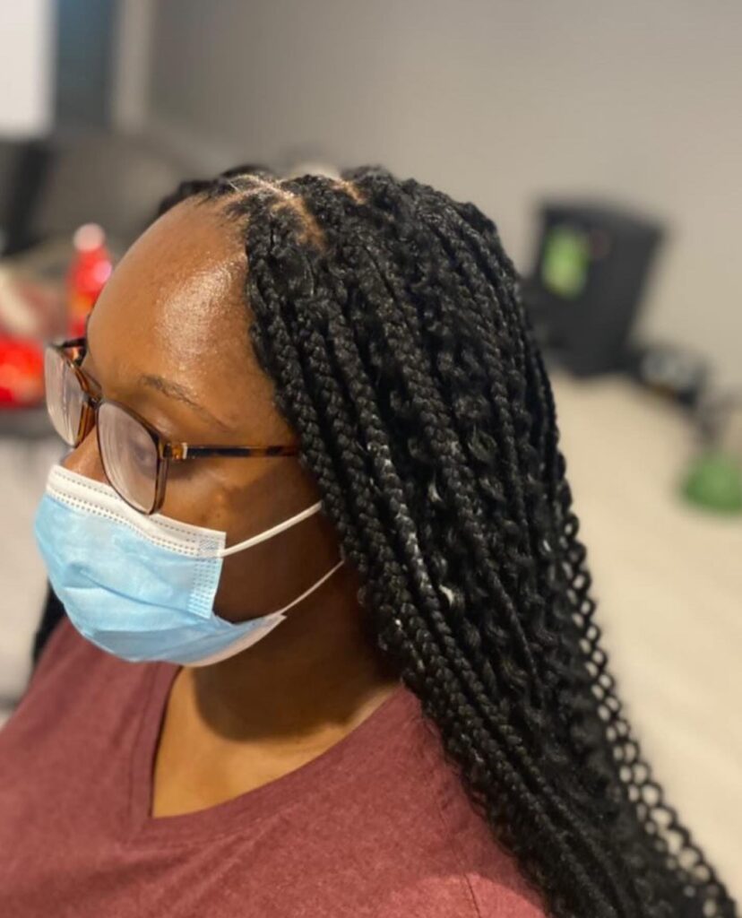 A woman wearing glasses and a face mask showing off her long and neat midnight black knotless braids.