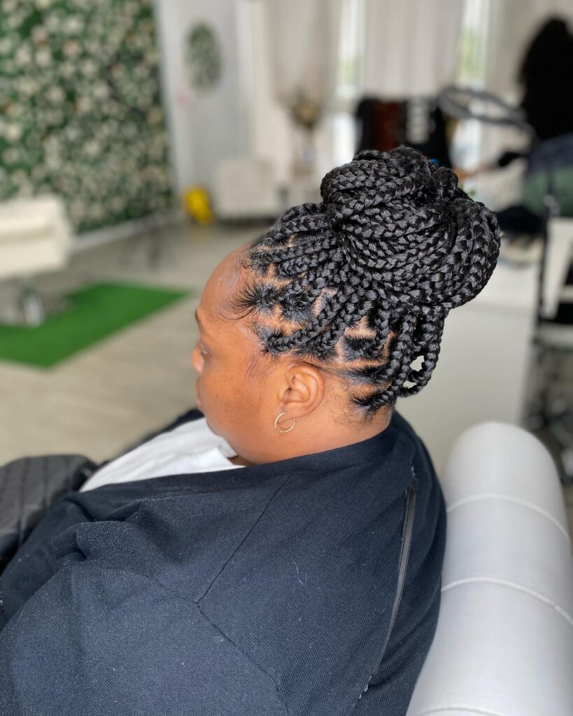 A woman from the side showing a large high bun made of thick black box braids with styled edges.