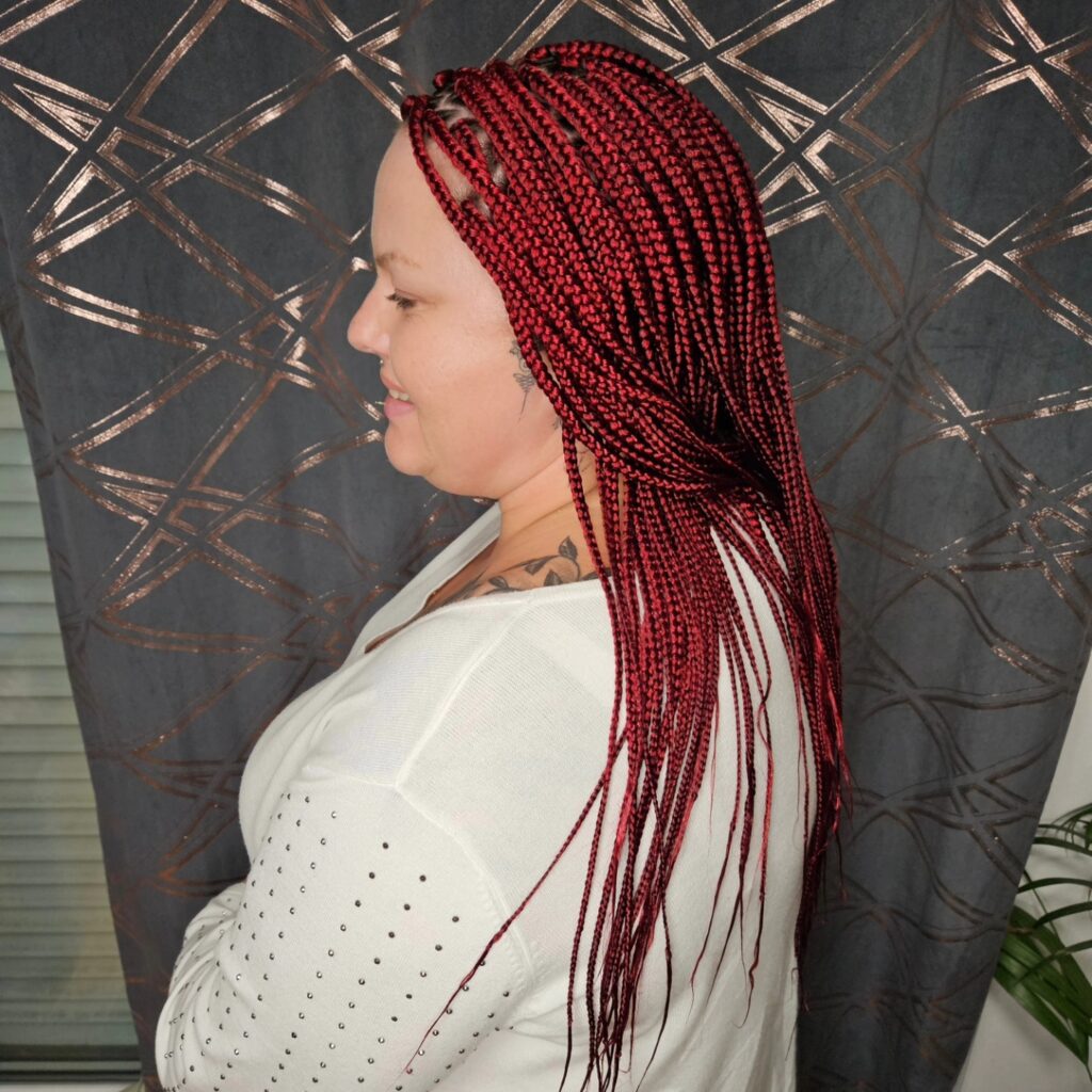 A woman in profile smiling and wearing long ruby red box braids that fall past her shoulders.