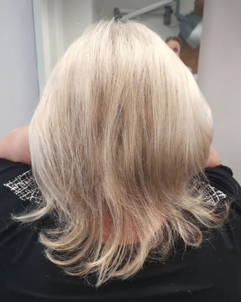 A rear view of a woman with thin hair wearing a champagne blonde lob with soft wispy layers and flicked out ends.