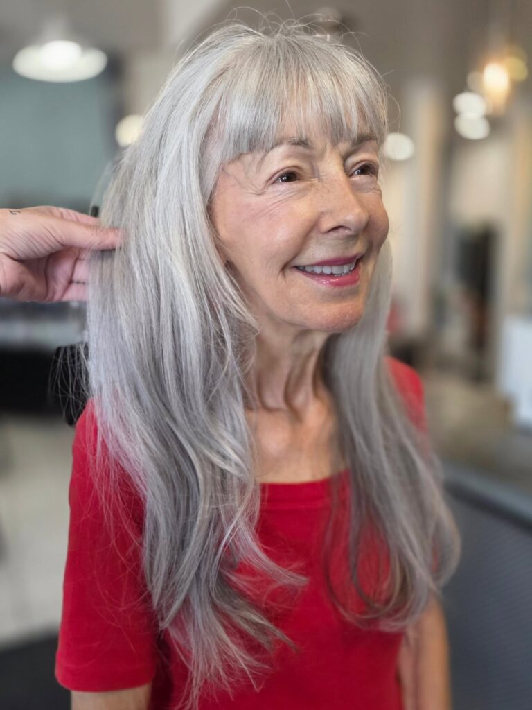 A woman with very long straight silver hair and blunt bangs smiling while wearing a red shirt.