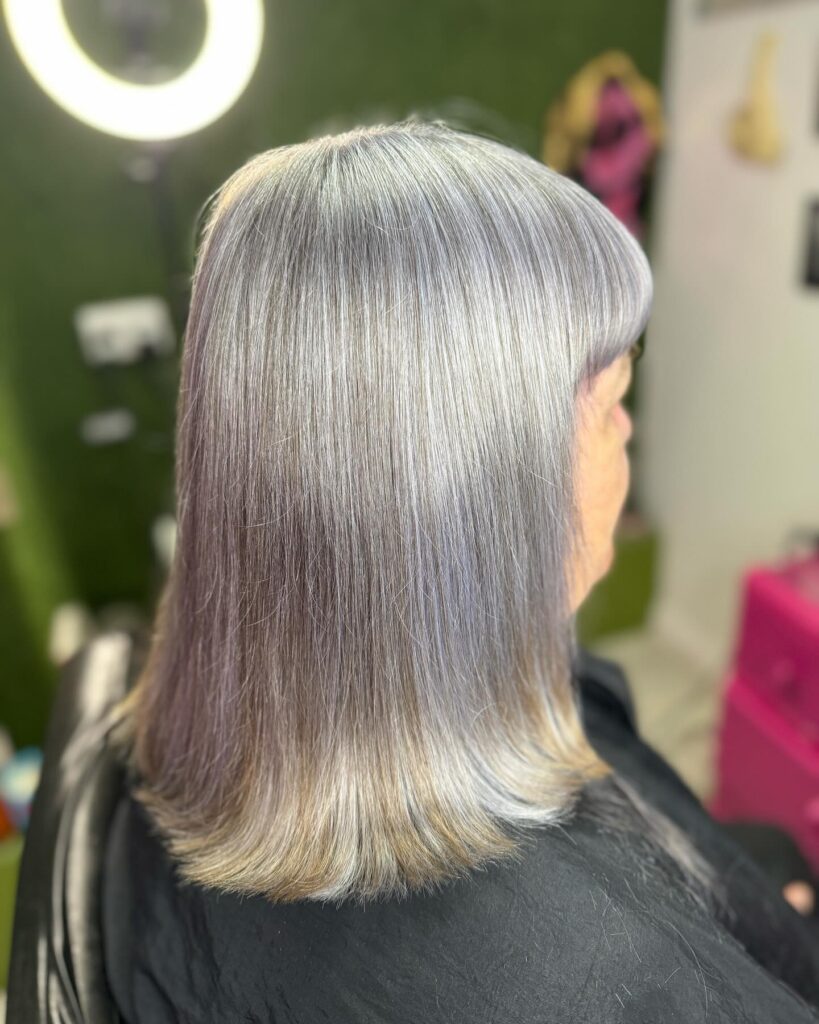 A woman with a shoulder length straight silver lob featuring subtle lavender highlights and a soft fringe.