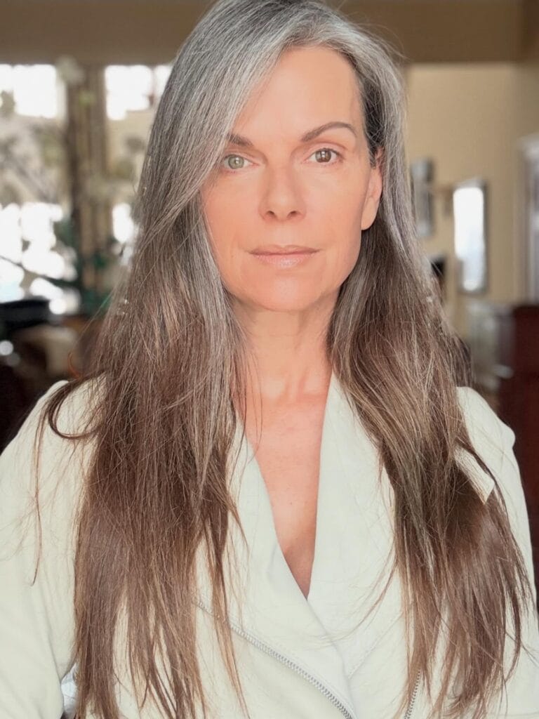 A woman with very long salt and pepper hair featuring a natural straight texture and silver highlights at the hairline.