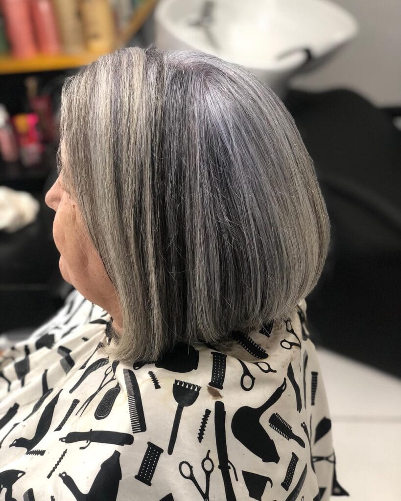 A side view of a woman in a salon cape with a straight chin length salt and pepper bob.