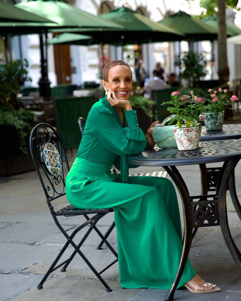 A woman sitting at an outdoor cafe sporting a very short and even buzz cut in a warm brown tone.