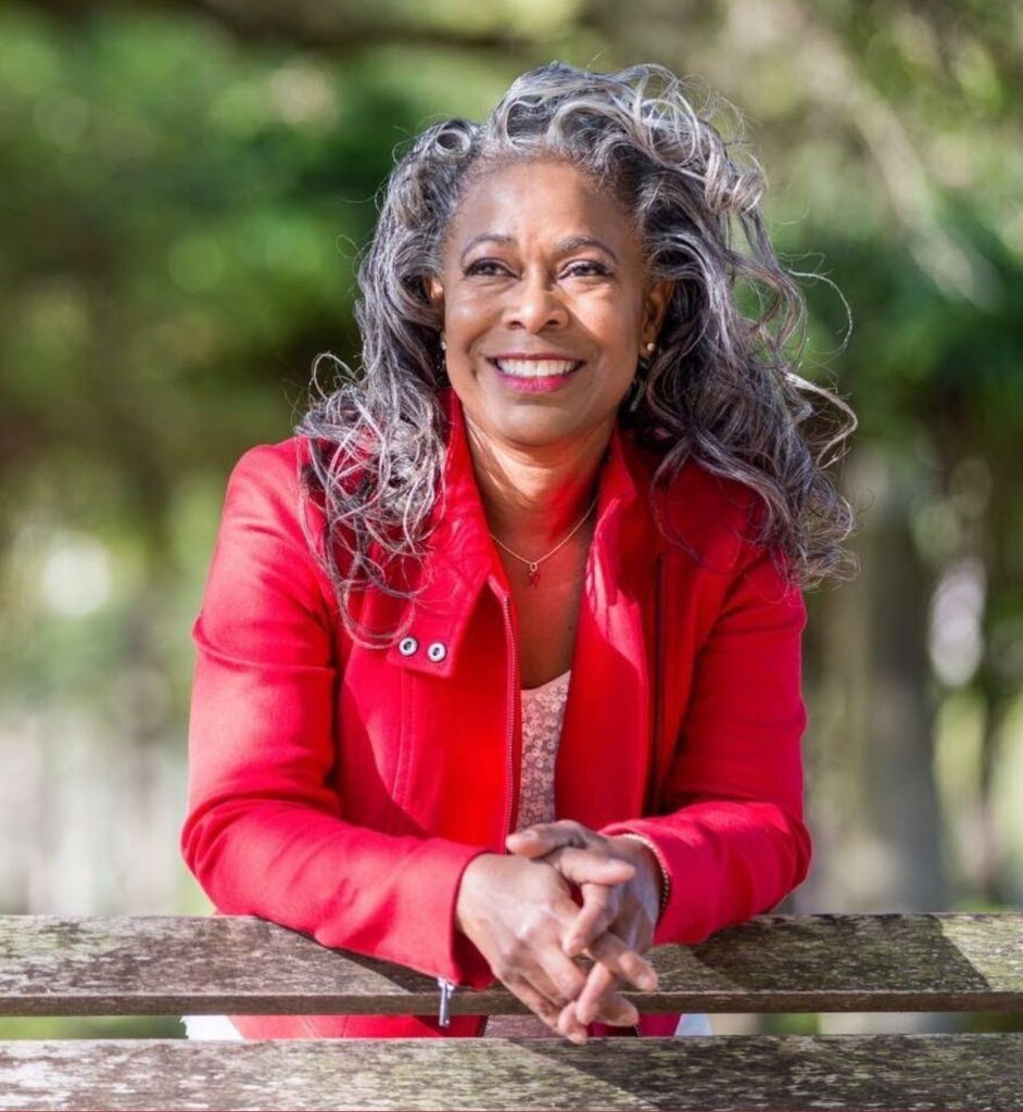 A woman with a bright smile wearing a shoulder length silver and charcoal curly hairstyle.