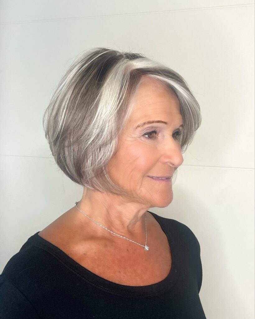 A woman with an oval face showcases a sleek inverted ash brown bob with a prominent silver money piece framing her face.