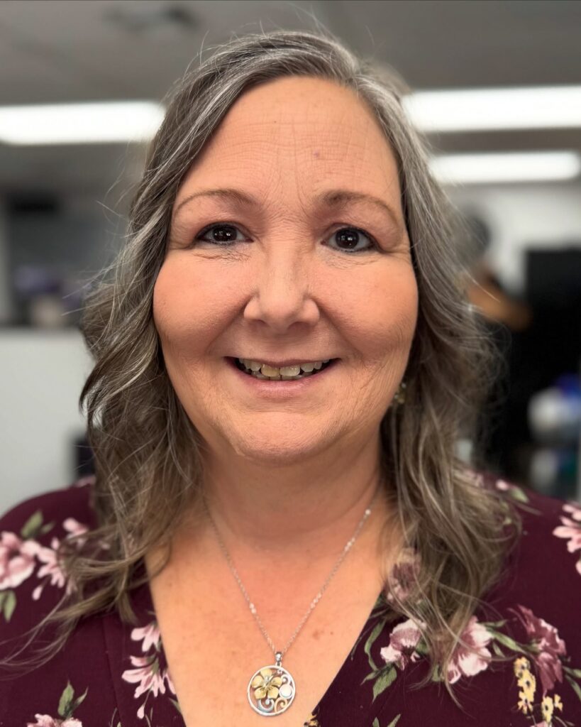 A woman with an oval face wears her ash blonde and silver hair in a mid length style with soft face framing waves.