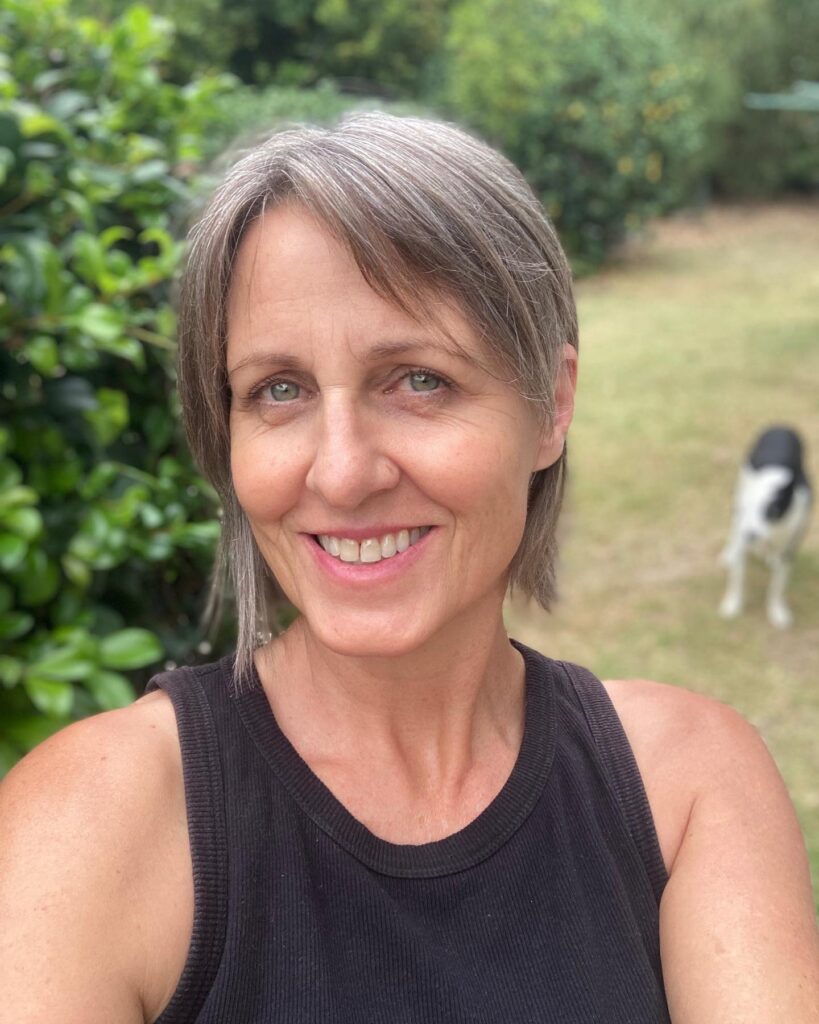 A woman with a sleek, straight ash gray bob cut with a side part, smiling in an outdoor setting.