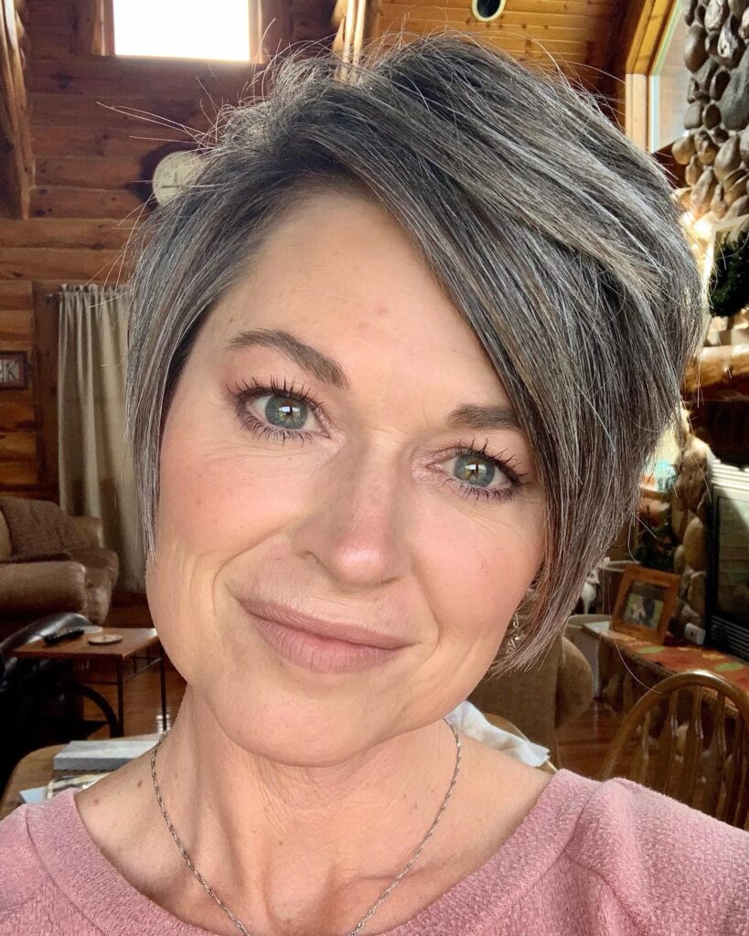 A woman with a straight asymmetrical silver and charcoal pixie cut styled with a dramatic side sweep.