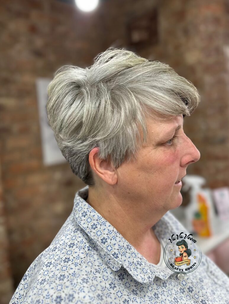 A side profile of a woman with a long face wearing a short silver pixie cut with textured layers swept back.