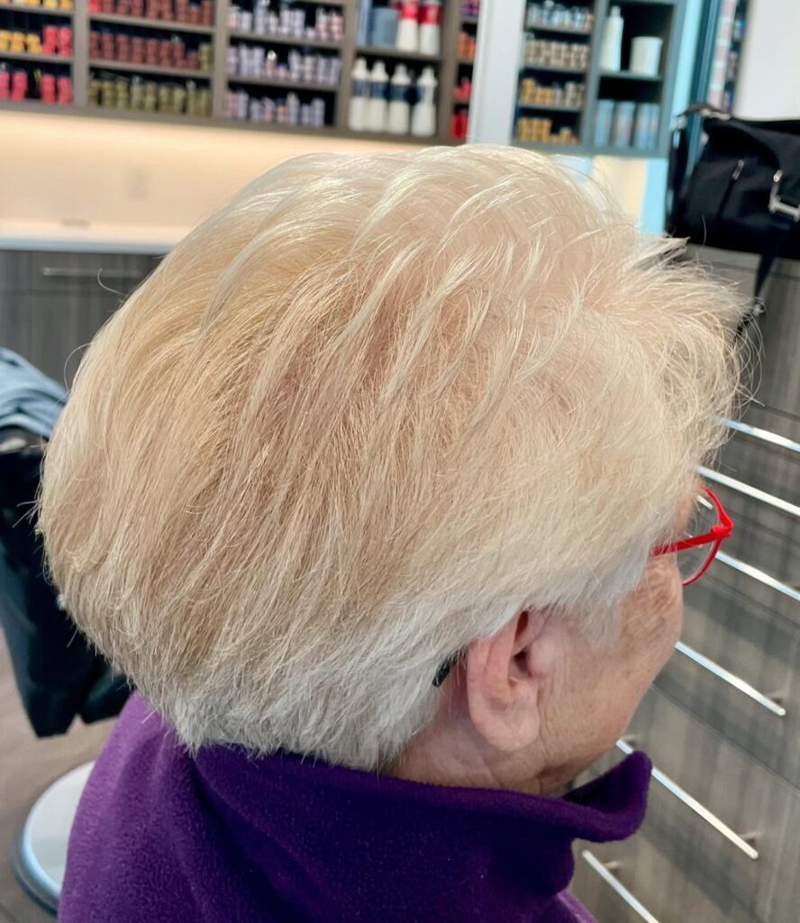 A woman viewed from the side with a short tapered pixie cut in a soft champagne blonde and white color.