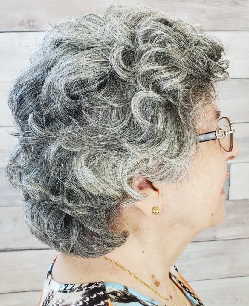 A woman with thick salt and pepper hair styled in a voluminous curly bob with short textured layers.
