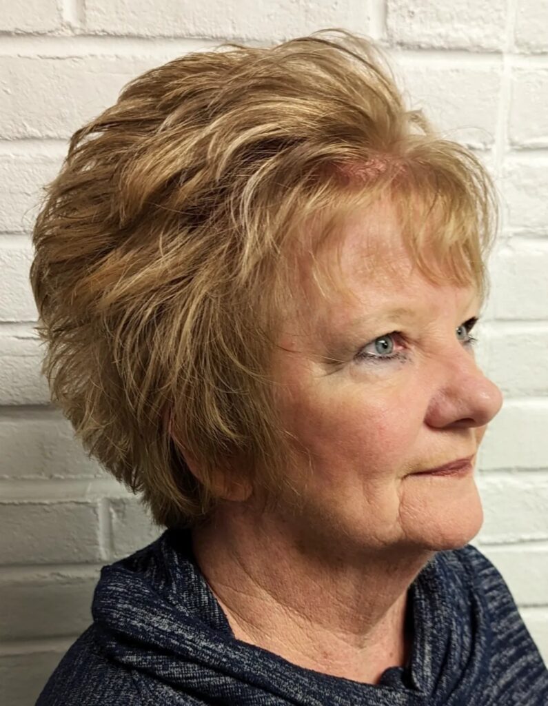 A woman with thick strawberry blonde hair styled in a voluminous layered pixie cut with soft bangs.