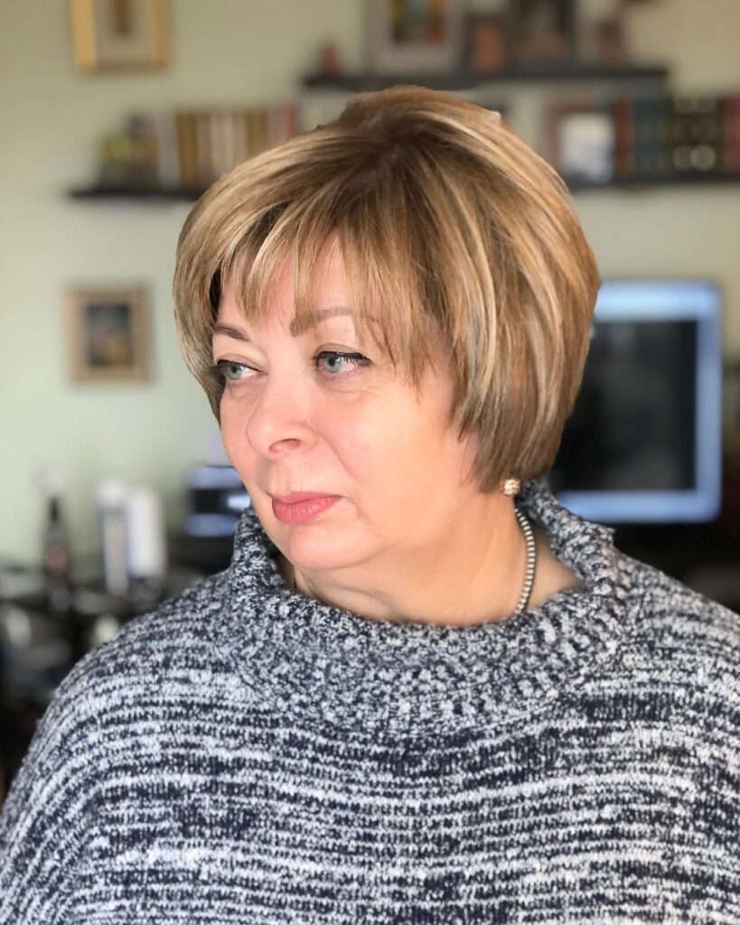 A woman with dimensional bronde hair styled in a voluminous, rounded pixie bob with fine textured bangs.