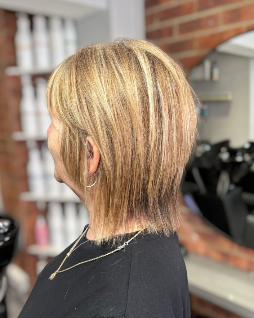 A side view of a woman with a sandy blonde shoulder length bob featuring shaggy layers and fine highlights.