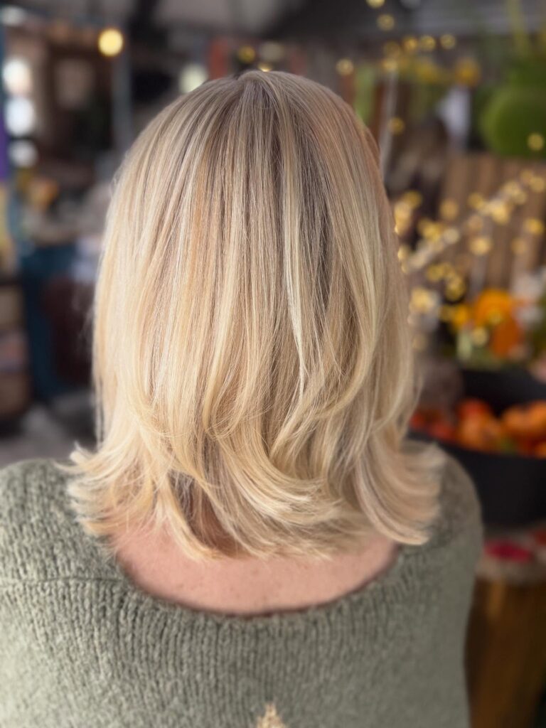 A back view of a woman with thick shoulder length creamy blonde hair featuring soft layers and upturned ends.