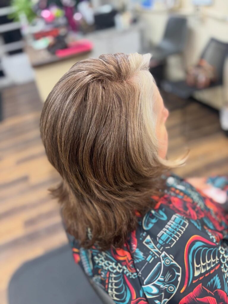 A woman with thick layered brunette hair features a prominent icy silver money piece highlight and soft wavy ends.
