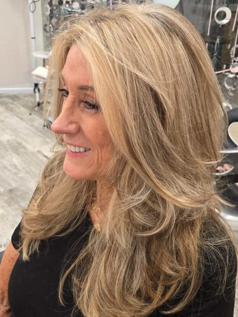 A woman with long thick golden blonde hair styled in voluminous face-framing layers and soft waves.