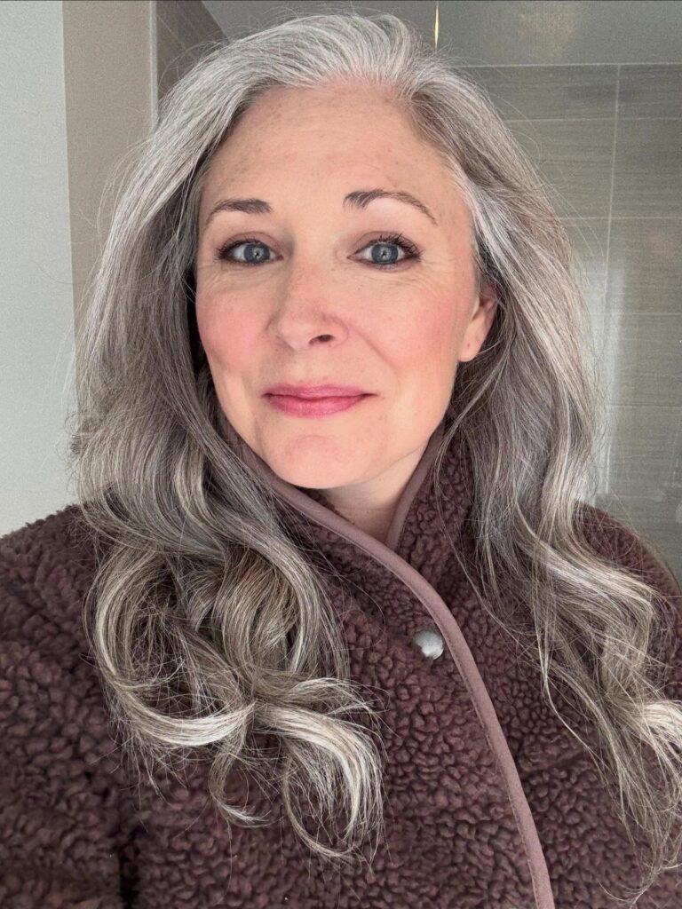 A portrait of an older woman with mid length wavy silver hair parted on the side smiling softly.
