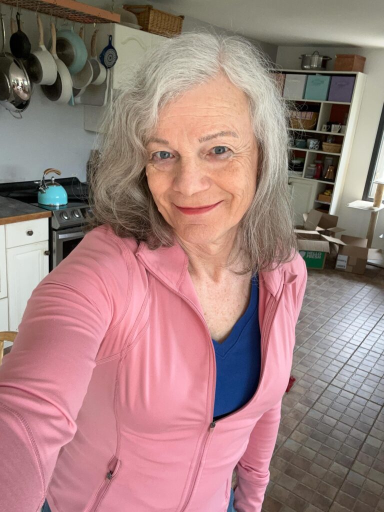 A portrait of a smiling woman in a pink jacket with a collarbone length wavy silver lob haircut.