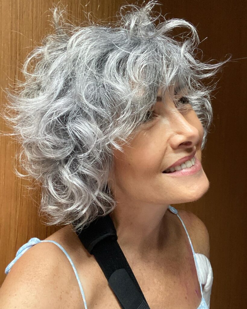 A portrait of an older woman with a vibrant natural silver curly chin length bob styled with lots of volume.