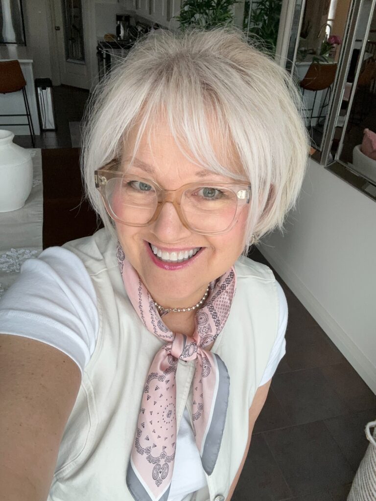 A smiling older woman wearing glasses with a bright platinum silver pixie bob hairstyle featuring wispy bangs.