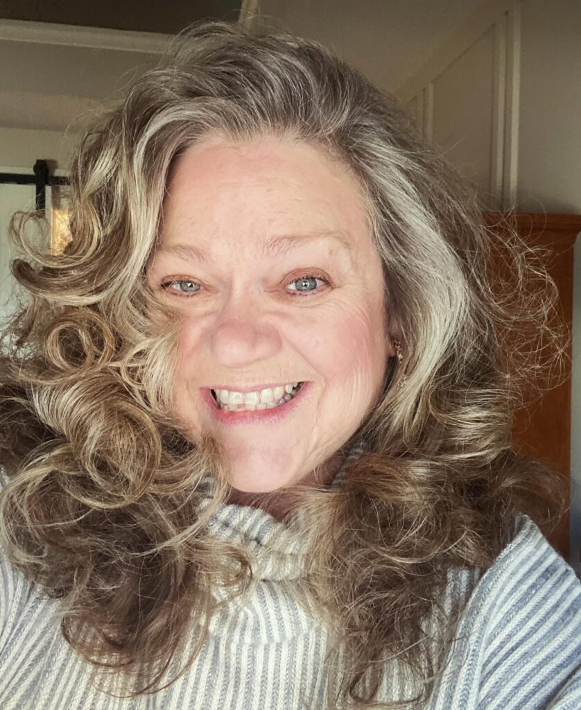 A portrait of a smiling woman with big voluminous beachy curls in warm brown and bright silver tones.