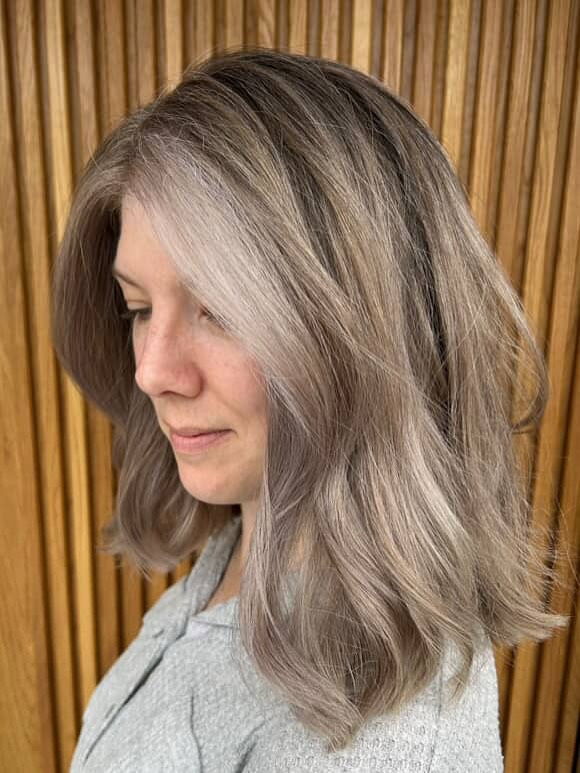 A woman with a neck length salt and pepper shag haircut featuring voluminous layers and a wispy fringe.