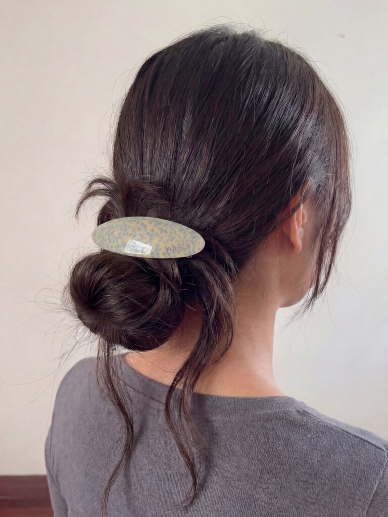 A woman with long dark hair styled in a messy low bun secured with a speckled oval barrette and loose tendrils hanging down.