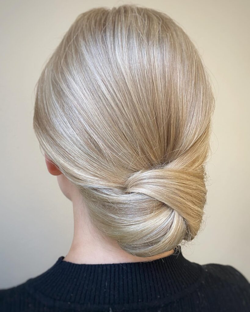A woman with sleek platinum blonde hair styled into an elegant twisted low chignon.