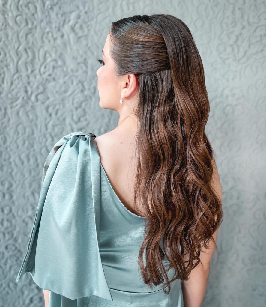 A woman with long dark brown hair styled in a sleek half up look with glossy tumbling waves.