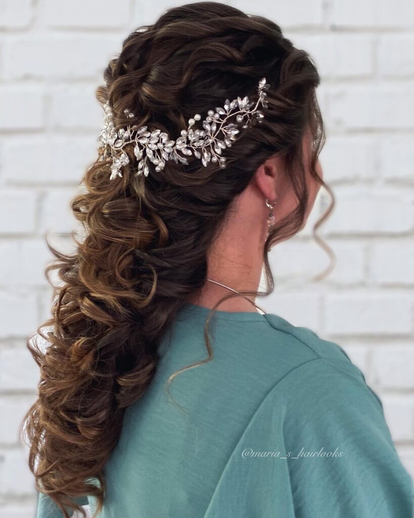 Rear view of a woman with long dark brown curly hair styled in a half up look adorned with a crystal leaf headpiece.