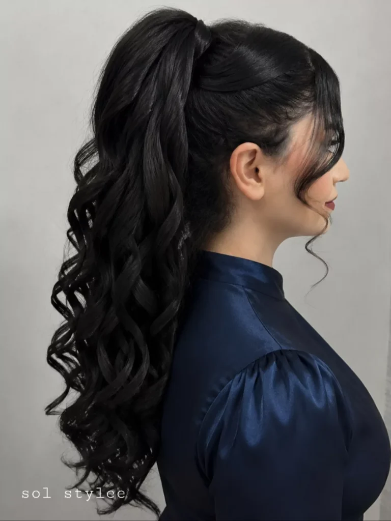 Side view of a woman with long black hair styled into a high voluminous ponytail filled with spiral curls and face framing tendrils.