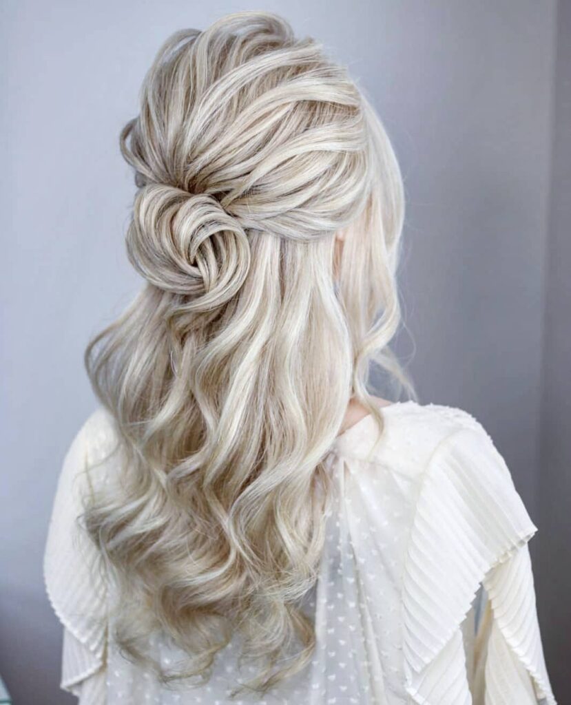 Three quarter rear view of a woman with long wavy platinum blonde hair styled into a textured half up twisted knot.