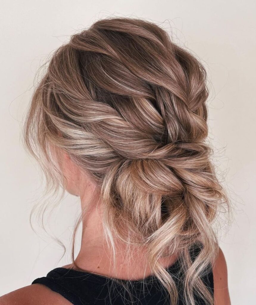 A woman with long highlighted ash blonde hair in a heavily textured low bun with twisted sections.