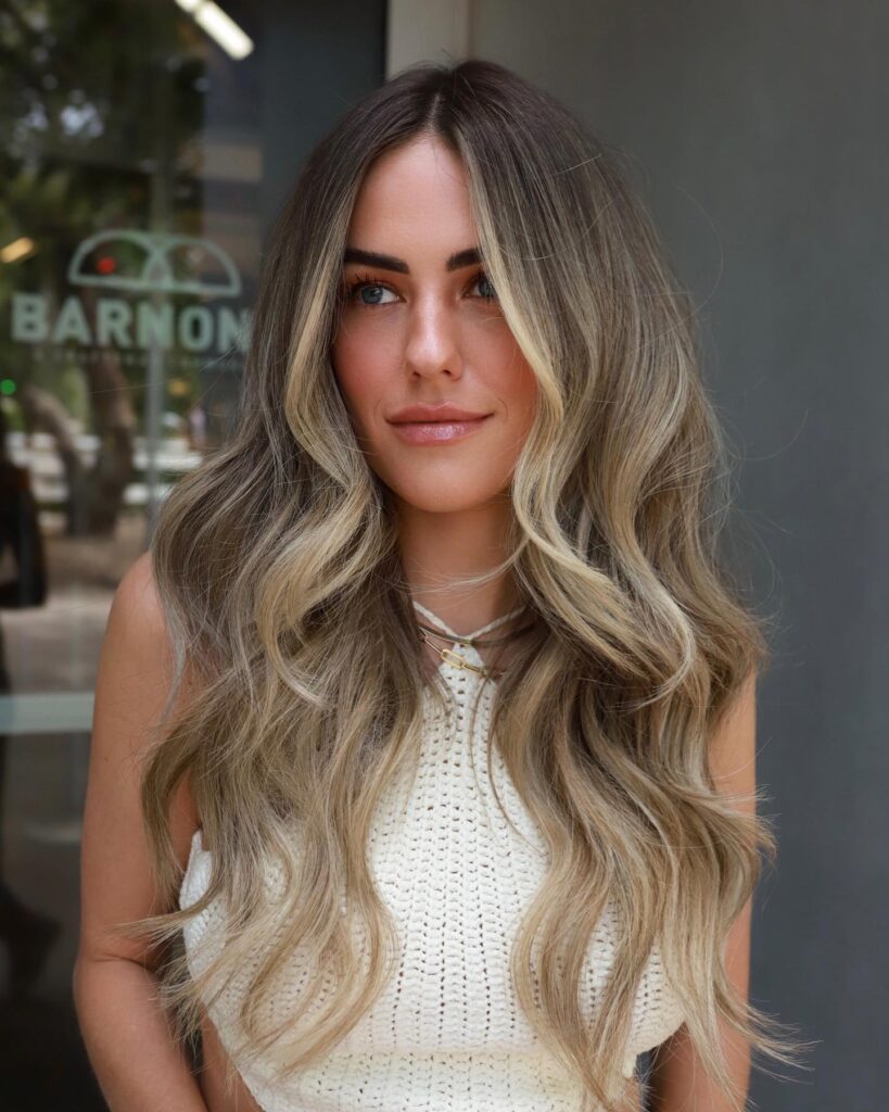 A woman with long wavy dark hair features ash blonde balayage and bright face framing money pieces.