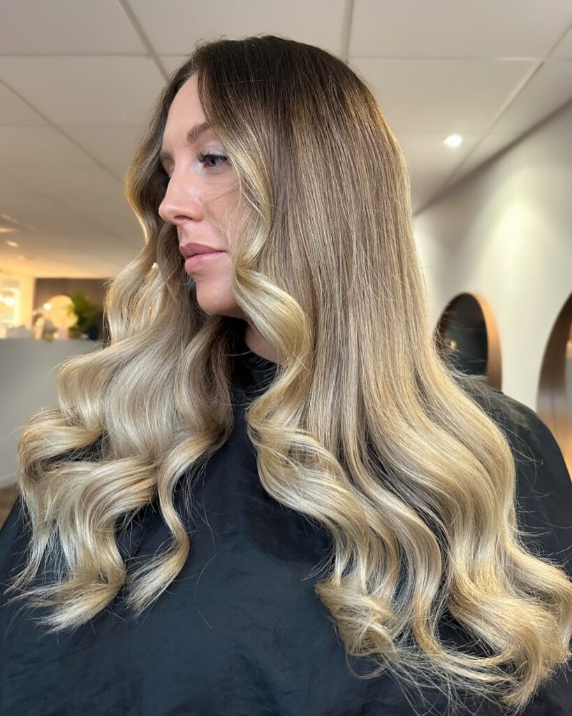 A woman with long, shiny sand blonde hair is showing off her glamorous large waves.