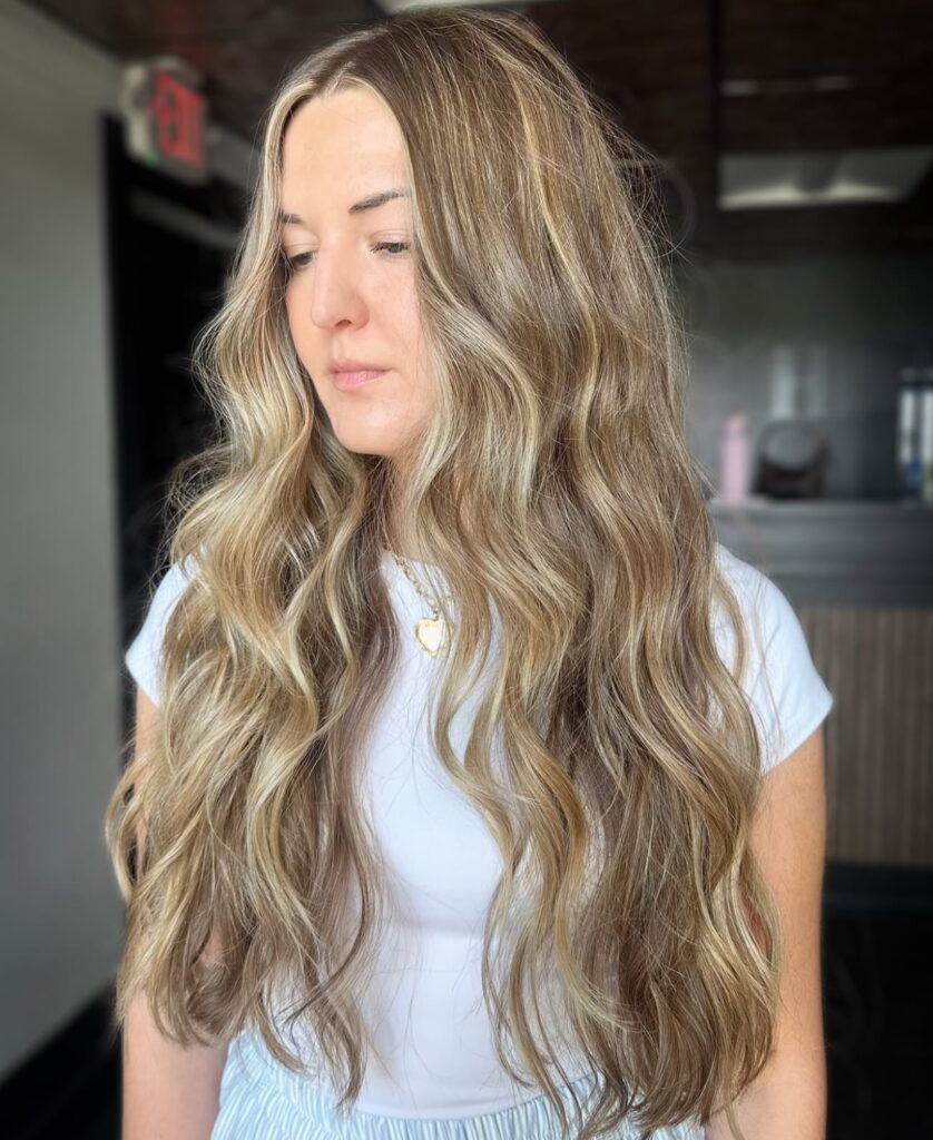 A woman with long flowing mermaid waves styled with fine golden blonde highlights and bright face framing pieces.